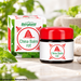 Bergland China Balm rot mit rotem Deckel und Verpackung in hellem Wellness-Ambiente mit frischen grünen Kräutern, Naturstein und weichem Hintergrund.