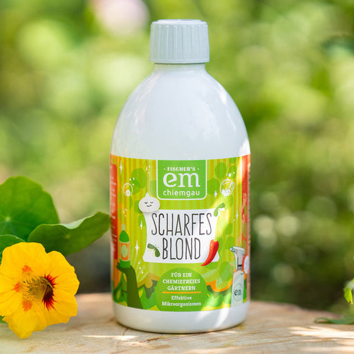 EM Chiemgau Scharfes Blond 500 ml Pflanzenpflegemittel mit Effektiven Mikroorganismen, fotografiert im Garten mit grünen Blättern und gelber Blüte.