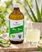 Golden Heart Aloe Vera Premium Direktsaft 500 ml mit einem Glas hellem Aloe-Vera-Saft und frischen Aloe-Vera-Blättern in natürlicher Umgebung.