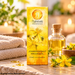 Nuhrovia Johanniskraut Massageöl 50 ml in gelber Verpackung, arrangiert mit Johanniskrautblüten, goldfarbenem Ölfläschchen, weichen Handtüchern und warmem Kerzenschein.