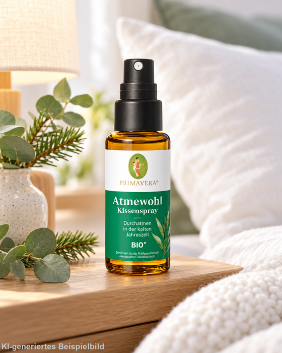 Primavera Atmewohl Kissenspray bio 30 ml auf einem hölzernen Nachttisch neben Eukalyptus und Tannenzweigen vor einem hellen Bett mit weichen Kissen.