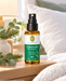 Primavera Atmewohl Kissenspray bio 30 ml auf einem hölzernen Nachttisch neben Eukalyptus und Tannenzweigen vor einem hellen Bett mit weichen Kissen.