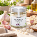 SalzManufaktur Knoblauch Saltini's im Glas in heller Küchenszene mit Knoblauchzehen, Salzstücken und Schale im Hintergrund.
