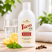 Young Living Thieves Fresh Essence Plus Mundspülung 236 ml in weißer Flasche mit cremefarbenem Originaletikett auf heller Holzoberfläche, umgeben von frischen Zitronen, grünen Minzblättern und Nelken, neben einem Glas mit klarer Flüssigkeit und weißem Handtuch im natürlichen Badezimmerambiente.