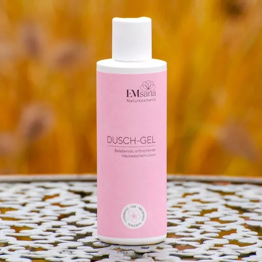 EMsana Dusch-Gel 200 ml in rosafarbener Flasche mit weißem Verschluss, freistehend auf dekorativem Untergrund vor warmem Hintergrund.